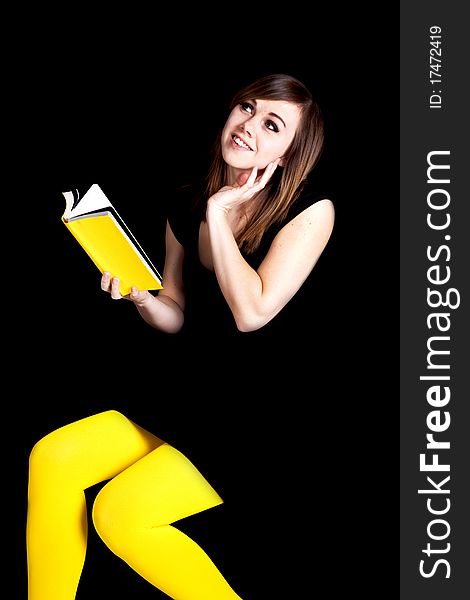A woman in front of a black background wearing yellow tights daydreaming about the yellow book she is reading. A woman in front of a black background wearing yellow tights daydreaming about the yellow book she is reading.