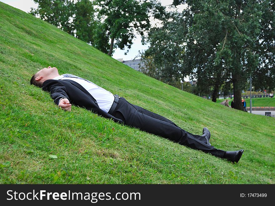 The young man in a jacket has a rest on a grass. The young man in a jacket has a rest on a grass