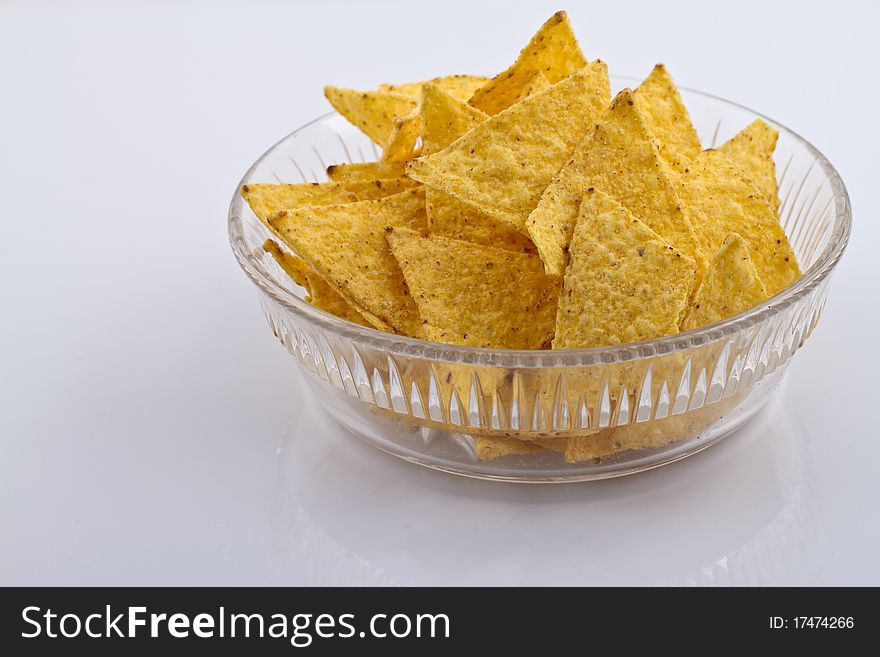 Glass bowl of nachos on white reflecting surface. Glass bowl of nachos on white reflecting surface