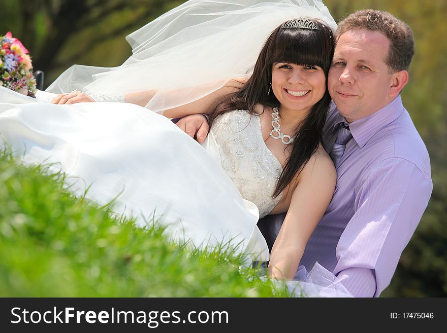 Happy groom and the bride sit on a grass