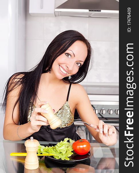 Beautiful young brunette woman eating vegetables in the kitchen at home