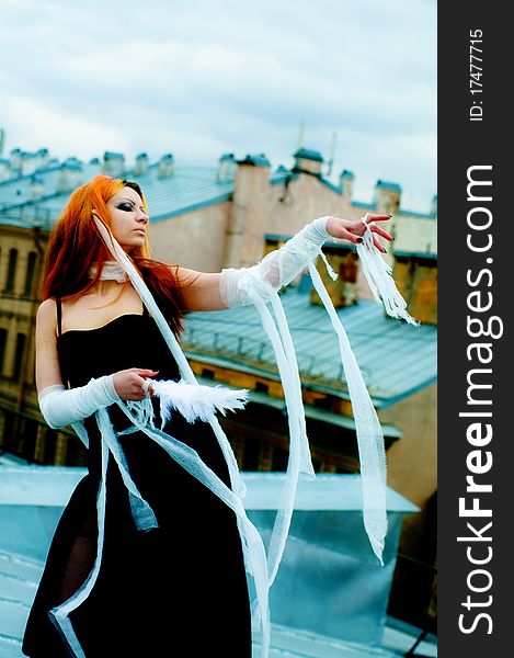 Photo of a Pretty red-haired girl with feathers, bandages and fan on rooftop