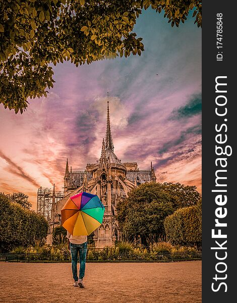 Young woman walking at Notre Dame Paris France ,sunset colors Notre Dame Paris, rainbow umbrella during sunset