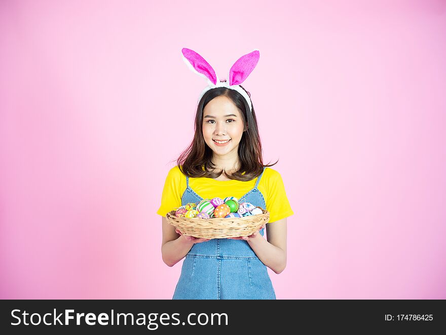 Half length studio shot of asian beauty happy young woman wearing bunny ears and holding colorful Easter egg in wood basket with lovely smile and colorful decor costume isolated on pastel backgrounds. Half length studio shot of asian beauty happy young woman wearing bunny ears and holding colorful Easter egg in wood basket with lovely smile and colorful decor costume isolated on pastel backgrounds.