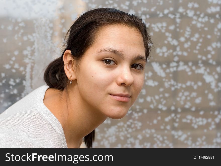 The young beautiful brown-eyed girl against a frosty window looks directly in the chamber. The young beautiful brown-eyed girl against a frosty window looks directly in the chamber