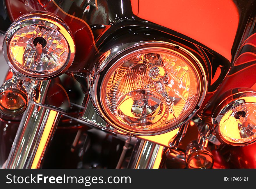 Close up shot of the headlights and part of the front shocks of a custom motorcycle in a hard orange lighted display. Close up shot of the headlights and part of the front shocks of a custom motorcycle in a hard orange lighted display