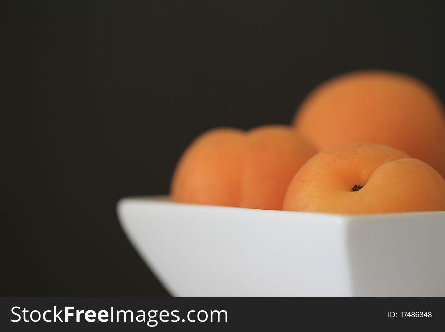 Fresh orange apricots on a small white bowl on black background. Fresh orange apricots on a small white bowl on black background