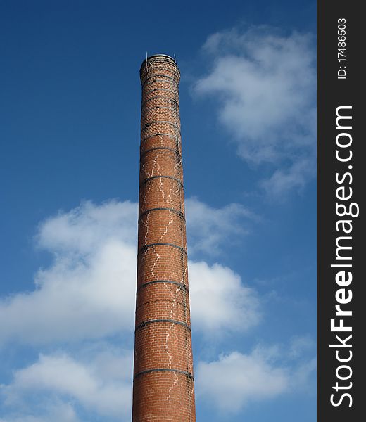 A old, cracked smokestack set against a blue sky with fluffy clouds