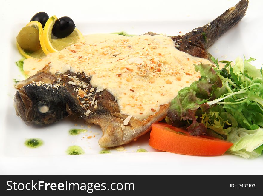 Fried fish with cream sauce with herbs, tomatoes, olives and lemon