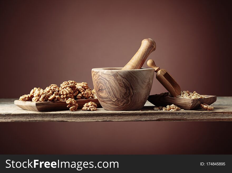 Walnuts in a wooden dish on an old wooden table. Crushed and whole nuts near the mortar. Brown background, copy space. Walnuts in a wooden dish on an old wooden table. Crushed and whole nuts near the mortar. Brown background, copy space