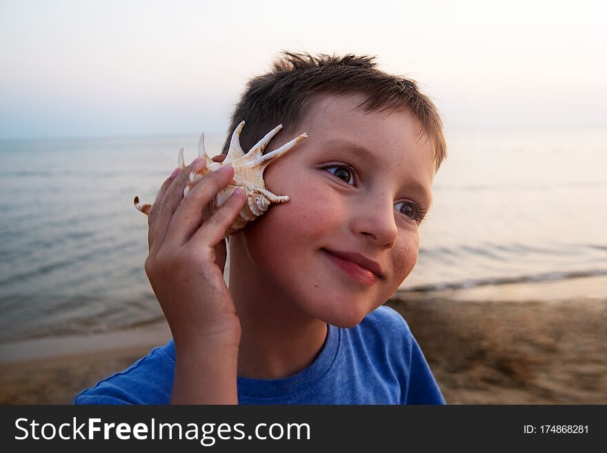 Pensive boy listens to a seashell on the seashore. Good hearing concept.
