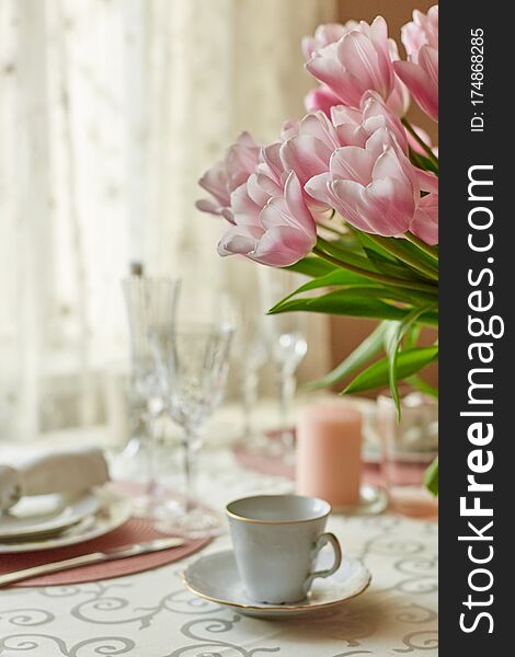 Decor and spring table setting is a vase with pink tulips and dishes of white color. Selective focus.