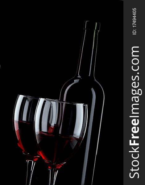 Bottle and glass of red wine on black background