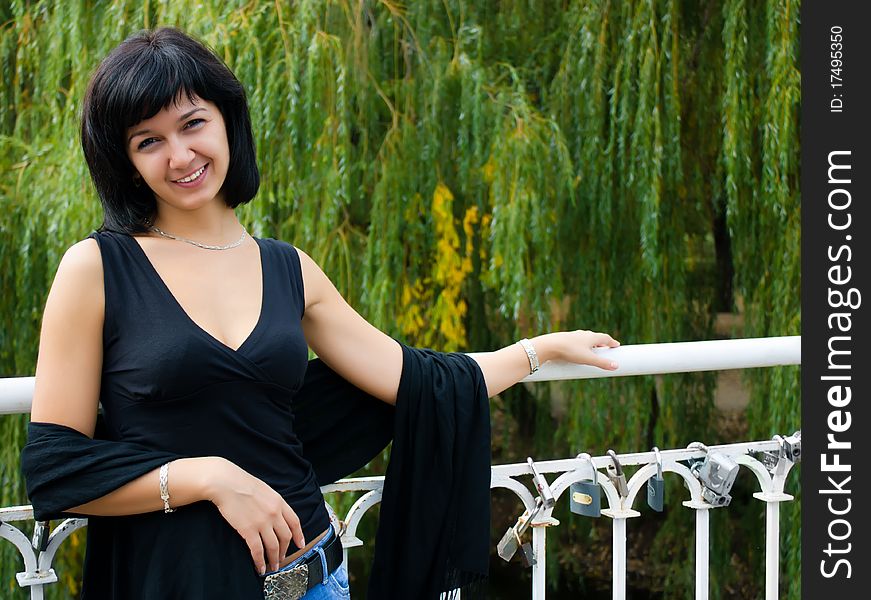 Smiling girl standing on the bridge on the background of green trees. Smiling girl standing on the bridge on the background of green trees