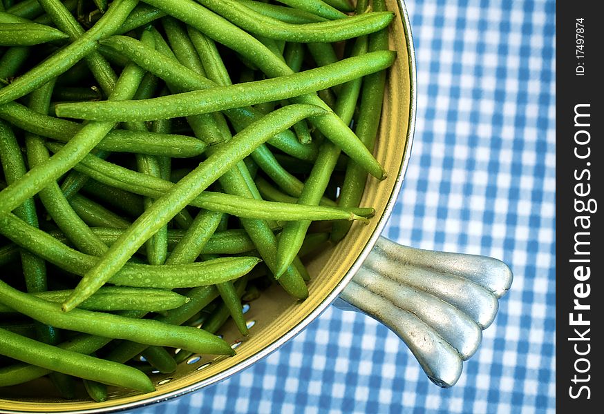 A colander of washed green beans in a blue checked tablecloth.