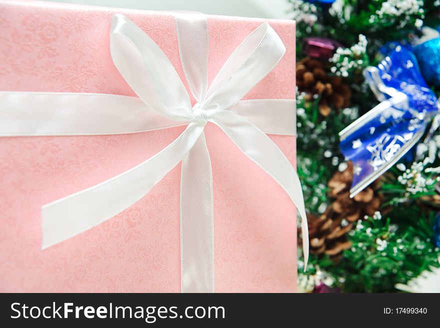 Pink christmas gift box front of a christmas tree