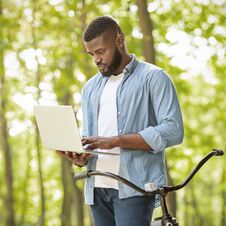 Rush Job. Focused Afro Businessman Standing Outdoors And Using Laptop Stock Photo