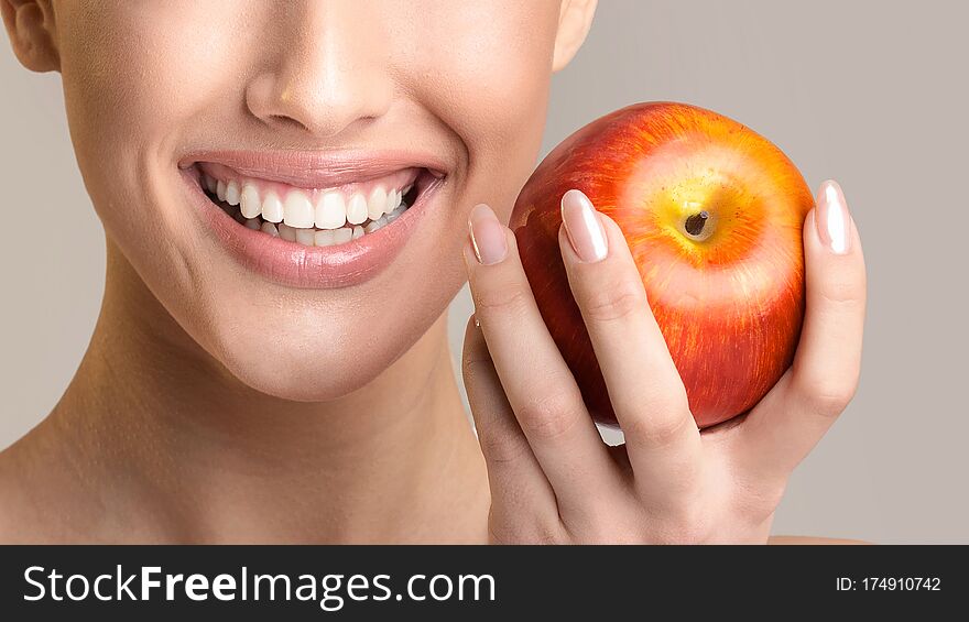 Toothcare. Unrecognizable Girl With Perfect Healthy Teeth Holding Red Apple And Smiling Posing Over Beige Studio Background. Panorama, Cropped. Toothcare. Unrecognizable Girl With Perfect Healthy Teeth Holding Red Apple And Smiling Posing Over Beige Studio Background. Panorama, Cropped