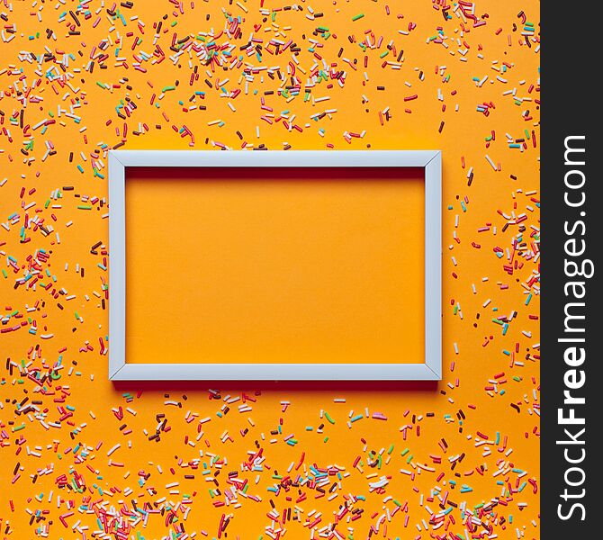 White frame and colorful sprinkles for cakes on orange background. Birthday party concept. Mock up, place for text