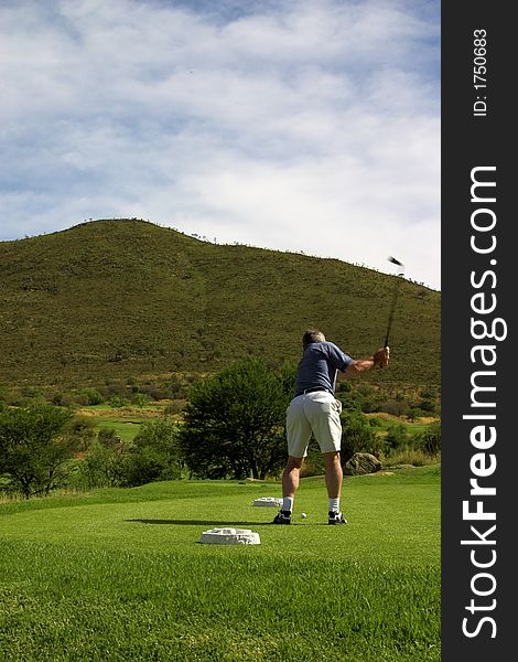 Golfer hitting a ball on the tee box. Club is in motion. Golfer hitting a ball on the tee box. Club is in motion.