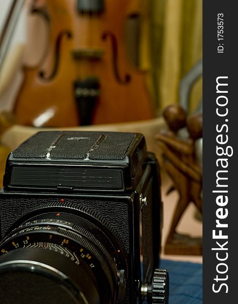 An old professional camera is partially shown in focus in the foreground while an off-focus violin stand behind it. An old professional camera is partially shown in focus in the foreground while an off-focus violin stand behind it.