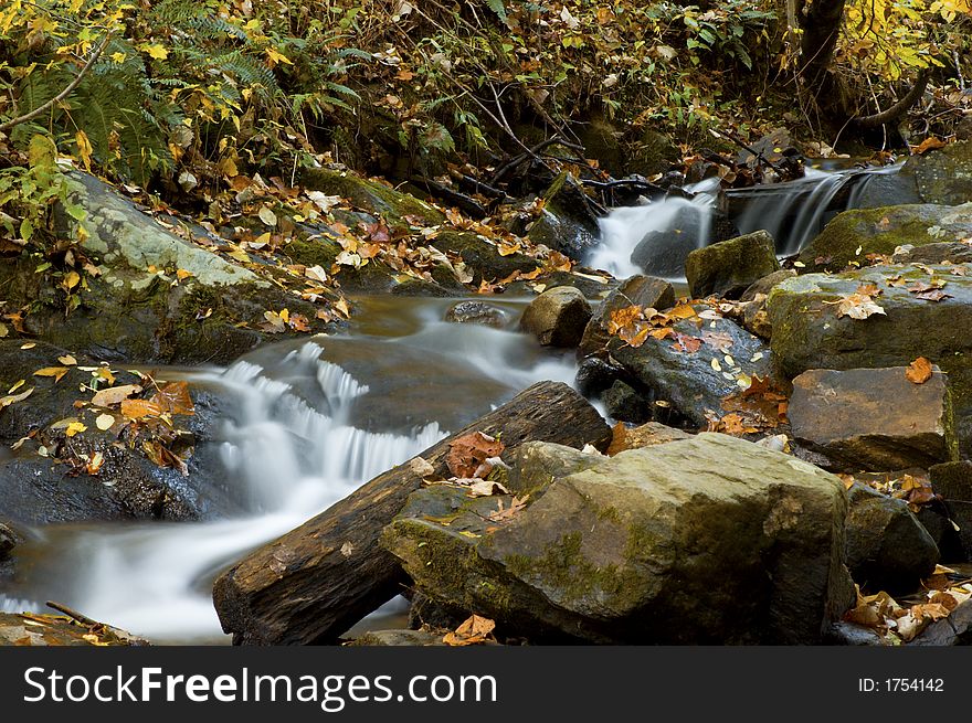 Small waterfall during the fall season with autumn color leaves and rocks framing the water. This photo was taken in the Georgian mountains. Small waterfall during the fall season with autumn color leaves and rocks framing the water. This photo was taken in the Georgian mountains.