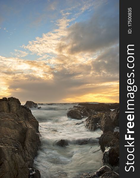 Sun setting over the ocean, with dramatic clouds overhead and rocks in the foreground. Sun setting over the ocean, with dramatic clouds overhead and rocks in the foreground