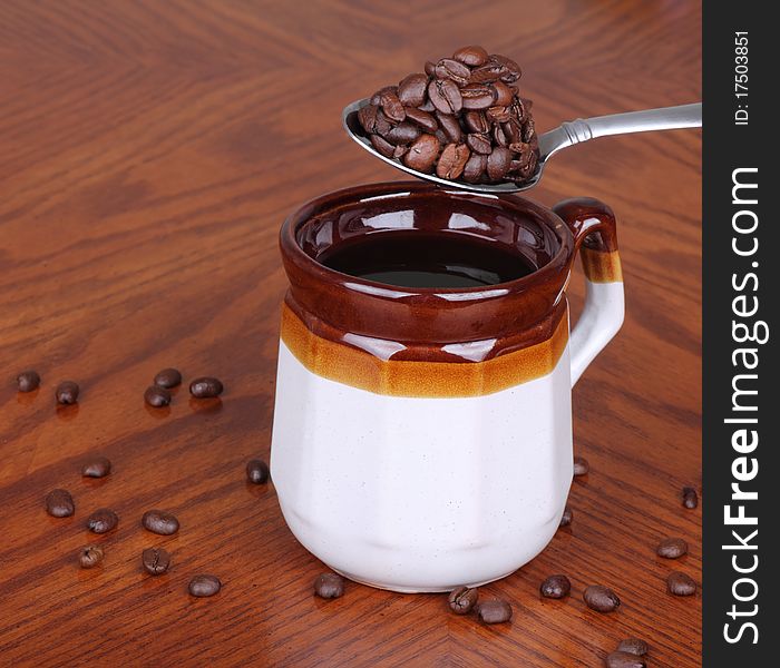 Heaping spoonful of coffee beans spilling around a cup of coffee. Heaping spoonful of coffee beans spilling around a cup of coffee