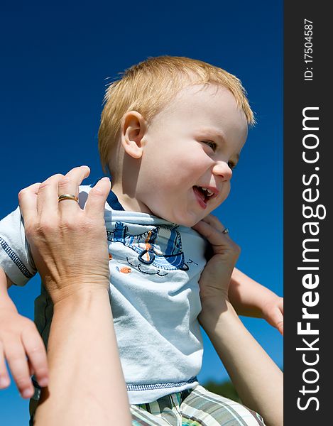 Laughing boy held up by his mother against blue sky. Laughing boy held up by his mother against blue sky