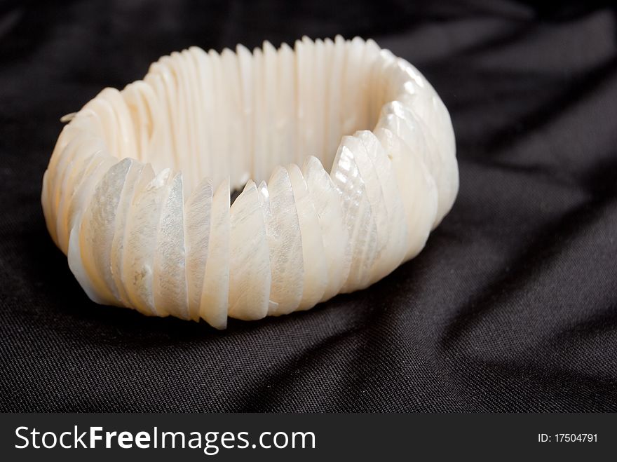 Bracelet from white cockleshells on a black fabric background. Bracelet from white cockleshells on a black fabric background