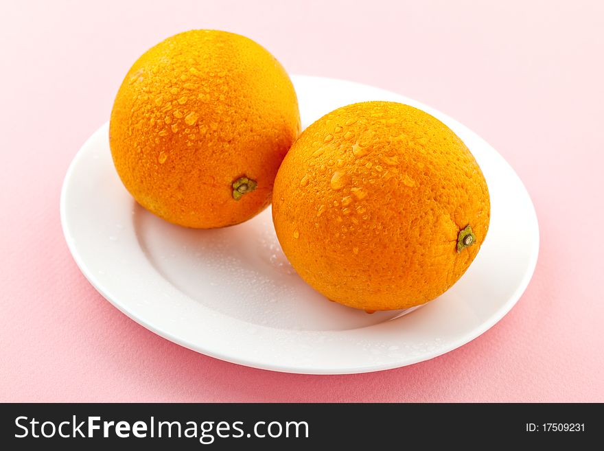 Ripe oranges with drops of water on a white plate