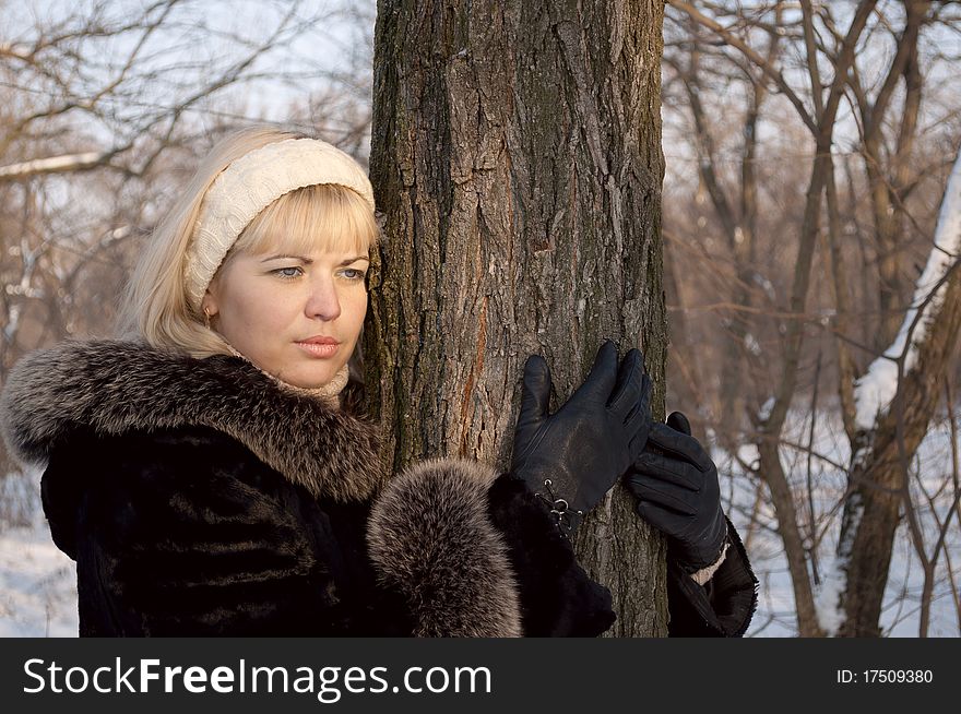 The thoughtful girl embraces a trunk of a winter tree. The thoughtful girl embraces a trunk of a winter tree