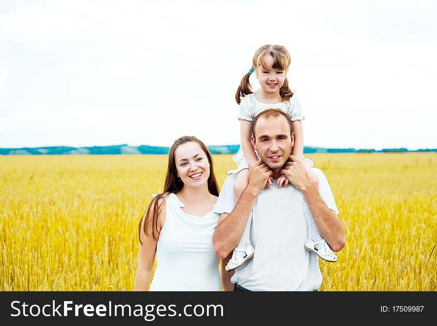 Happy family; young mother, father and their daughter having fun at the wheat field