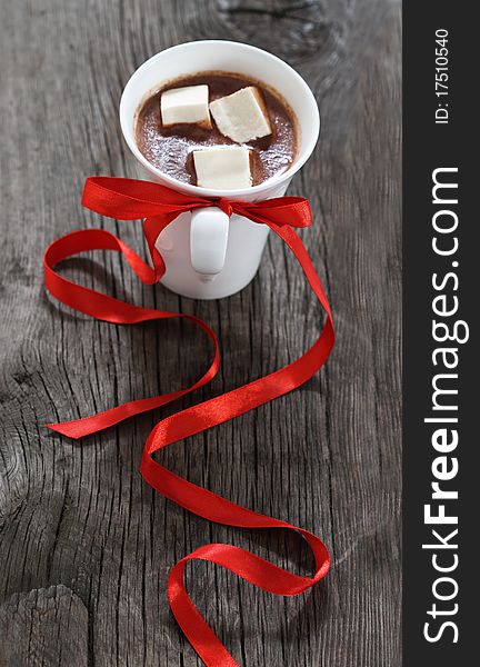 Mug of hot chocolate or cocoa with marshmallows decorated by red ribbon