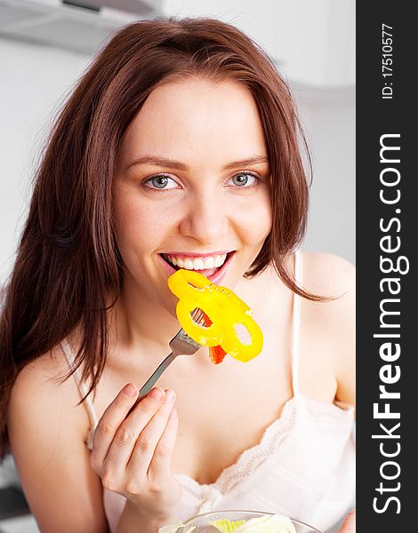 Beautiful young woman eating salad in the kitchen at home