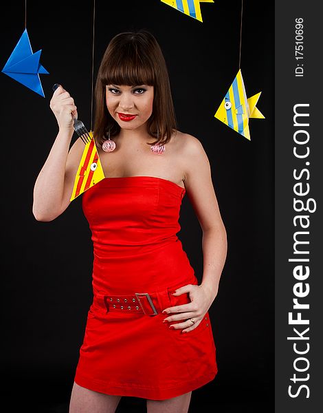 Beautiful girl in a red dress with paper fish and fork is isolated on a black background. Beautiful girl in a red dress with paper fish and fork is isolated on a black background