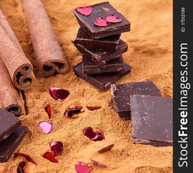 Chocolate pieces with cinnamon sticks and ground cinnamon, and heart shaped confetti. Chocolate pieces with cinnamon sticks and ground cinnamon, and heart shaped confetti