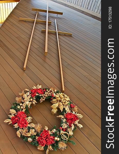 This stock image has three crosses with a view of looking up at the crosses from the foot of the cross inside a portion of a church. There is a gold and red Christmas wreath hanging beneath the crosses. This stock image has three crosses with a view of looking up at the crosses from the foot of the cross inside a portion of a church. There is a gold and red Christmas wreath hanging beneath the crosses.