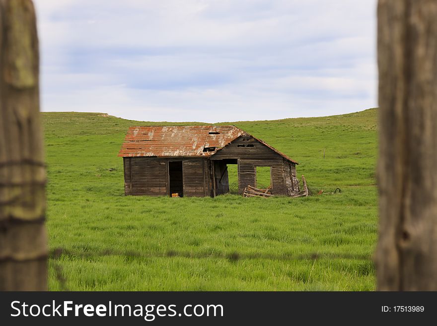 Image of an abandoned farmhouse framed between two fence posts. Image of an abandoned farmhouse framed between two fence posts.