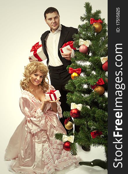 Victorian couple stand near a Christmas tree with gift boxes. Isolated over white background. Victorian couple stand near a Christmas tree with gift boxes. Isolated over white background
