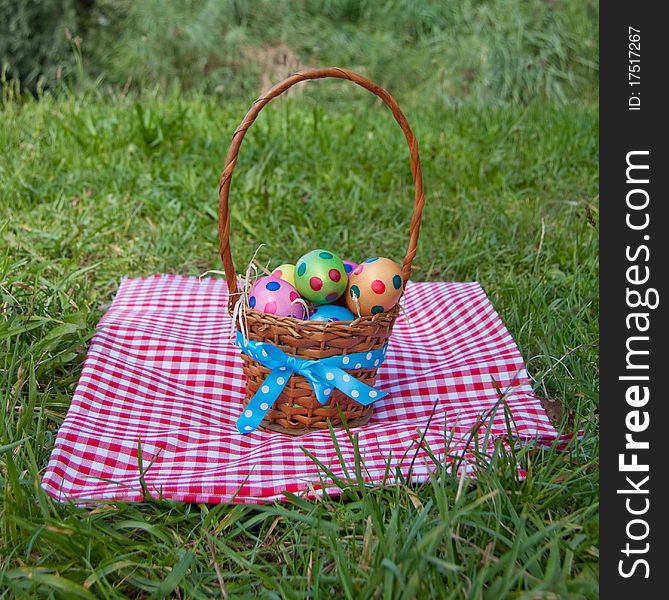 Colorful dotted easter eggs in a wicker basket on a green lawn