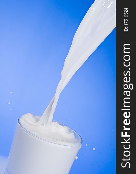 Pouring milk into a glass isolated over blue background