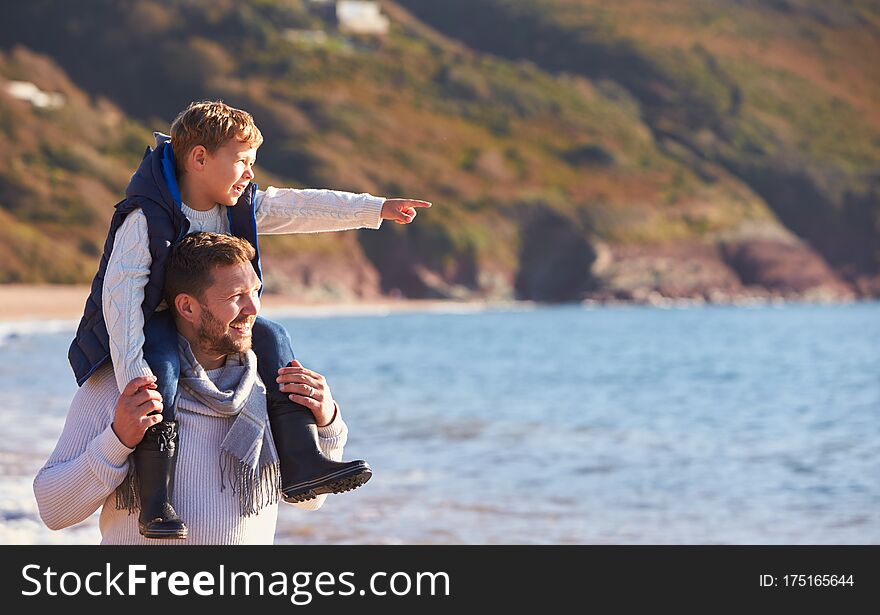 Father Giving Son Ride On Shoulders As They Walk Along Beach By Sea