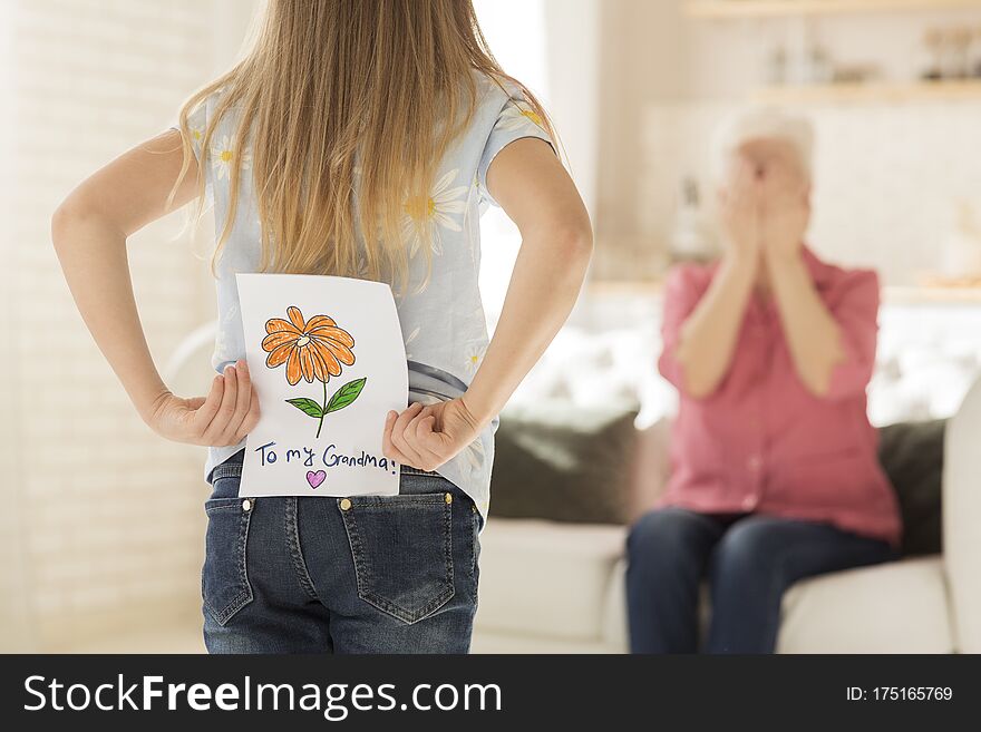 Family celebration. Little girl with greeting card for granny behind her back, closeup. Empty space