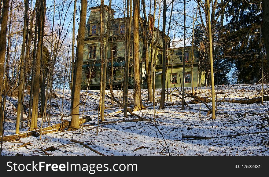 A view of a Victorian House Through Trees at the Top of a Hill