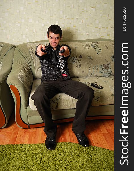 The young guy sits on a sofa with a control panel in a hand. The young guy sits on a sofa with a control panel in a hand