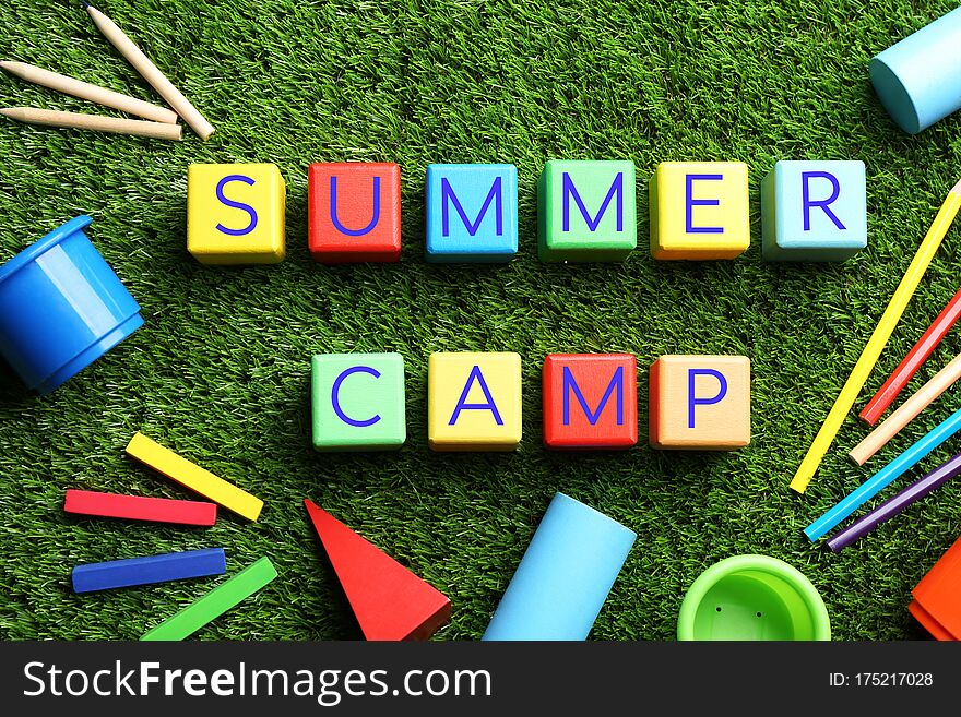 Flat lay composition with phrase SUMMER CAMP made of colorful cubes on green grass