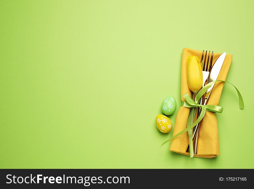 Top view of cutlery set with floral decor on green background, space for text. Easter celebration