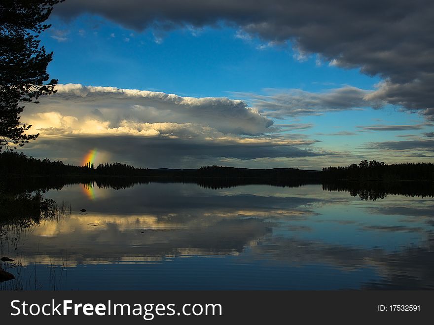 Strom rising over calm lake with gorgeous short rainbow.