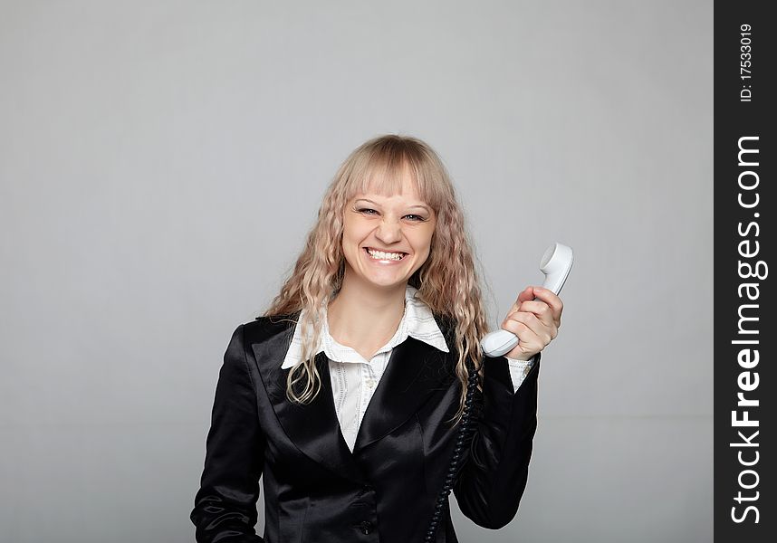 Funny business woman in a black suit with a gray background with the handset in the hands
